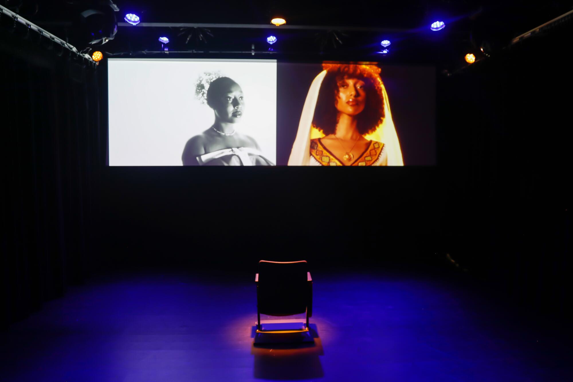 A two screen video installation in a dark room with a single chair in the middle 