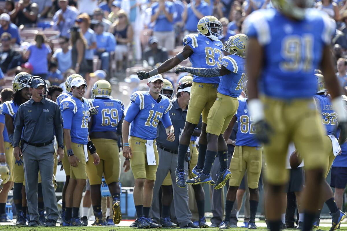 UCLA coach Jim Mora looks on as receiver Alex Van Dyke (83) chest bumps teammate Demetric Felton after his second-quarter touchdown against Hawaii at the Rose Bowl.