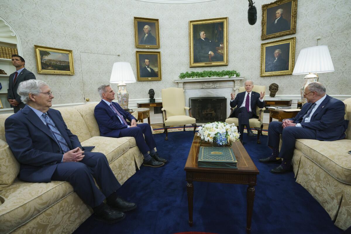 Four men in suits sit in an ornate room. 