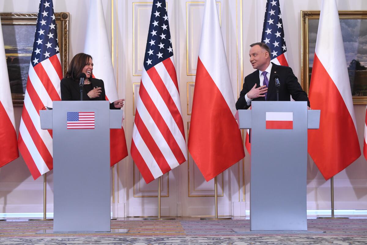 kamala harris and andrzej duda laugh and stand behind silver lecterns surrounded by American and Polish flags