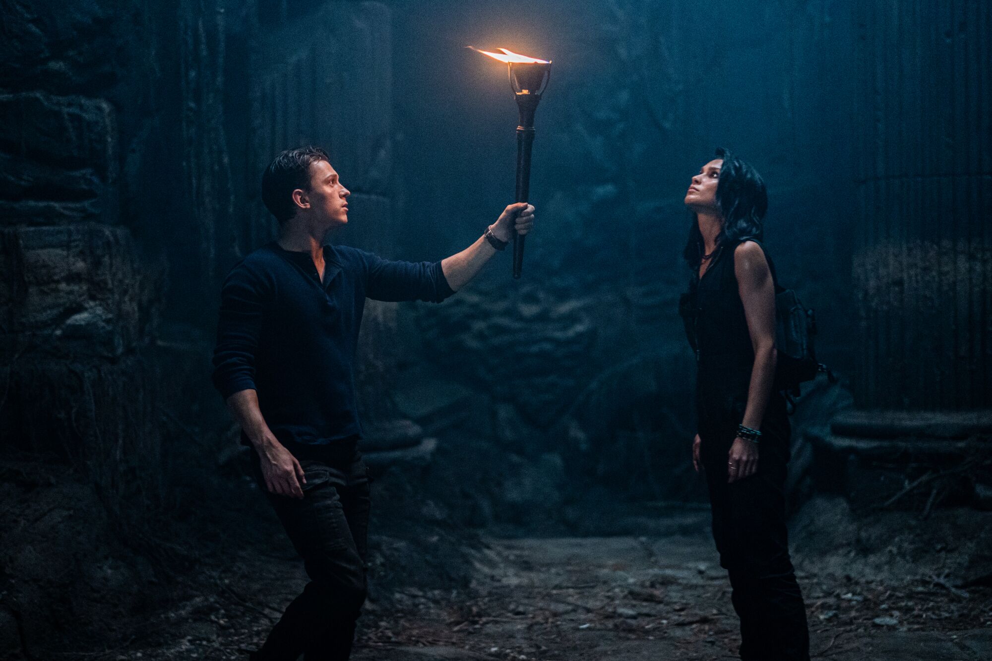 A man holds a torch in a dark space as he and a woman look around.