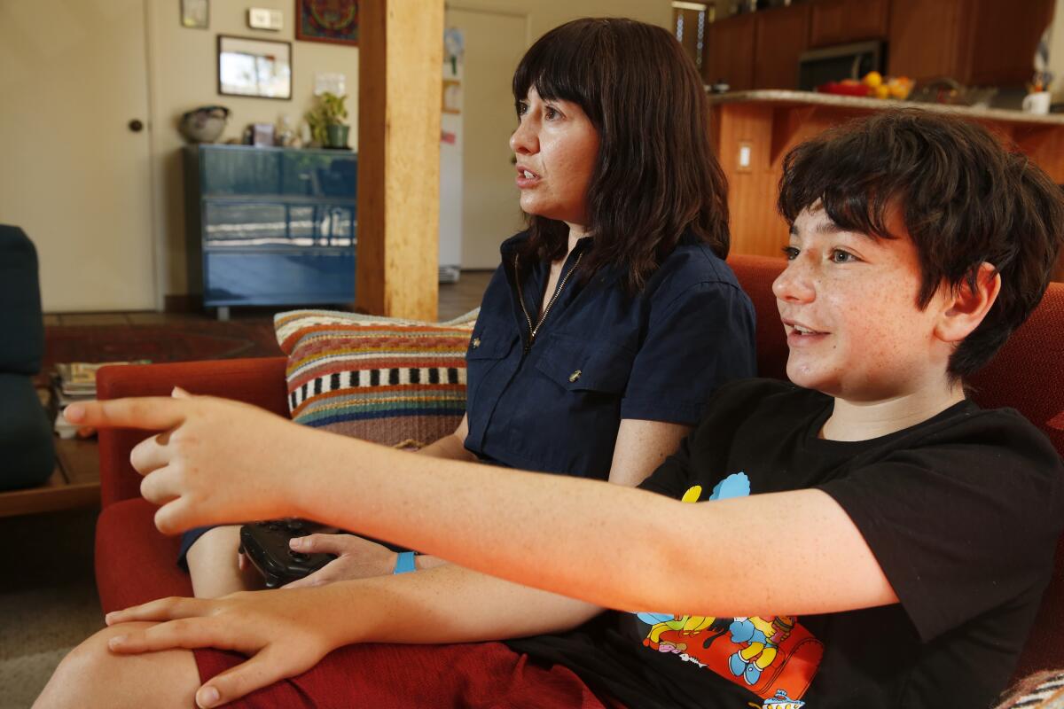 A woman and a boy play a video game sitting on a couch.