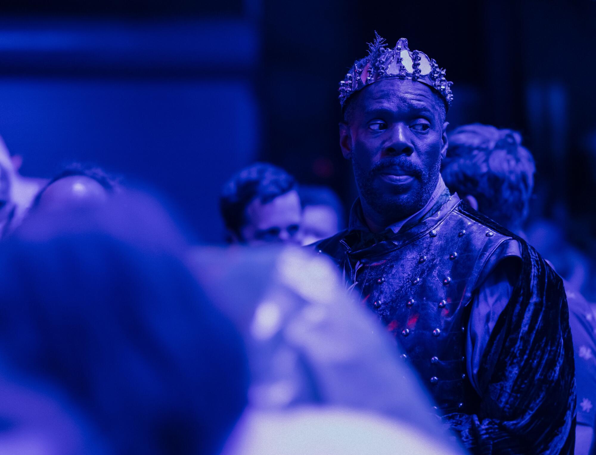 A performer in a crown watches.