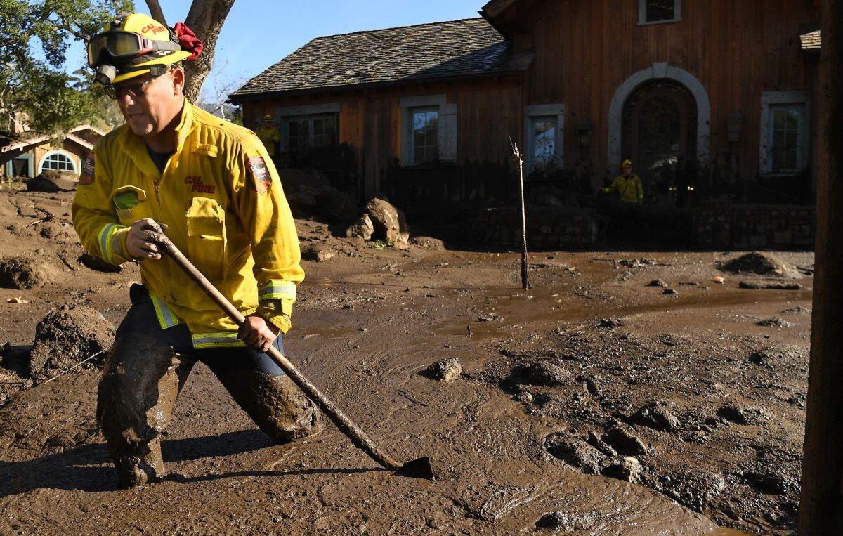 Cal Firefighter Alex Jimenez walk out of the mud after marking a spot with a stick where he found a body along Glen Oaks Drive in Montecito. (Wally Skalij/Los Angeles Times)