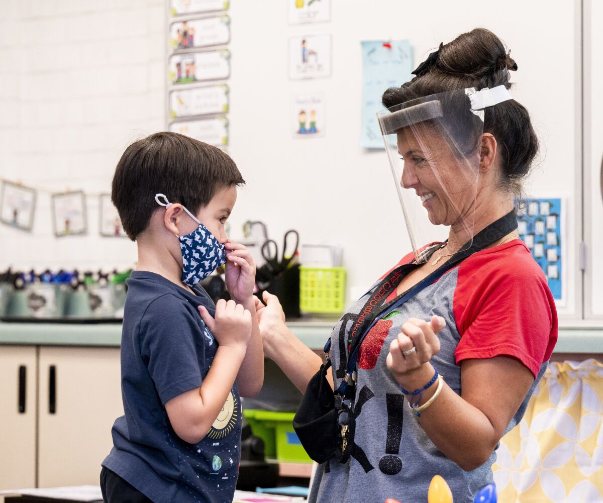 A student gets help with his mask from a kindergarten teacher.