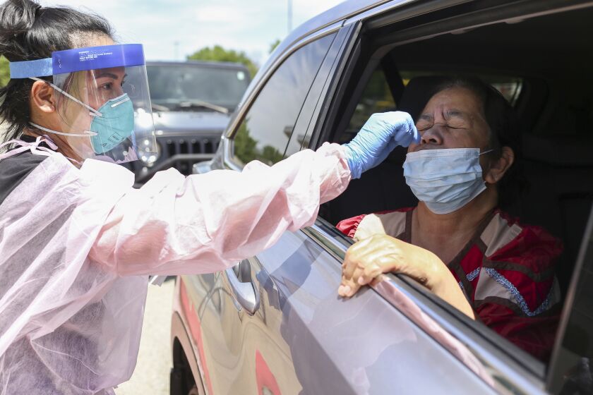 Nurse Ruby Lewis (from left) administers a covid-19 test to Laling Riklon of Springdale, Ark. at the Center for Nonprofits parking lot in Springdale, Ark., Saturday, May 23, 2020. The Arkansas Department of Health partnered with the Arkansas Coalition of Marshallese to host a drive-thru covid-19 testing site. Volunteers also distributed groceries and masks to those waiting in line. (NWA Democrat-Gazette/Charlie Kaijo)