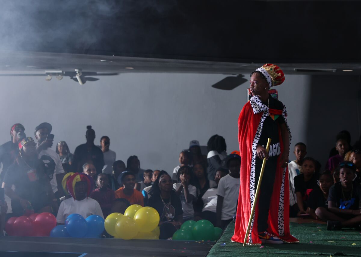 A boy dressed as a king standing on a stage, lit by a stage light to the left.