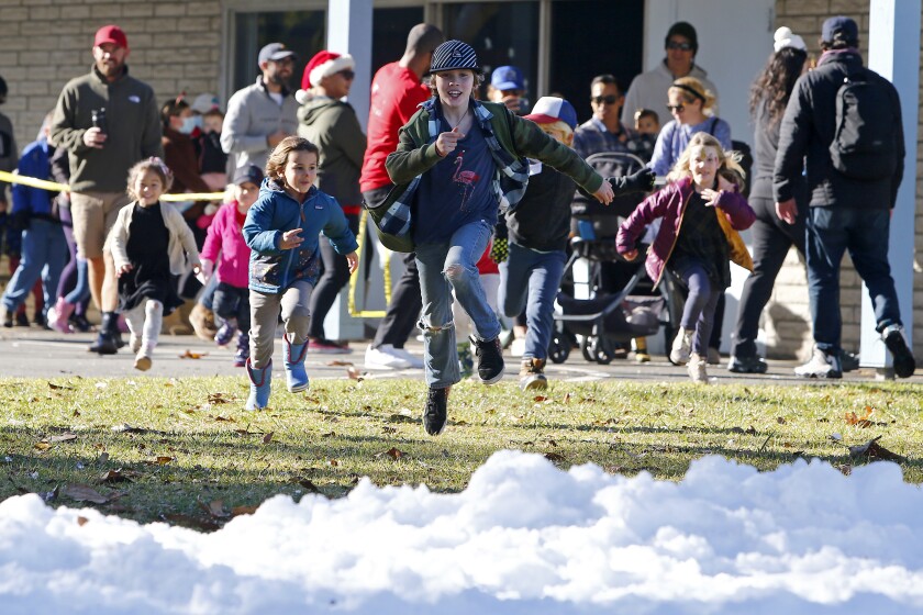 Ryder Kirkspiers, 10, center, sprints to the snow during the annual holiday Snow Land event on Saturday at Balearic Park.