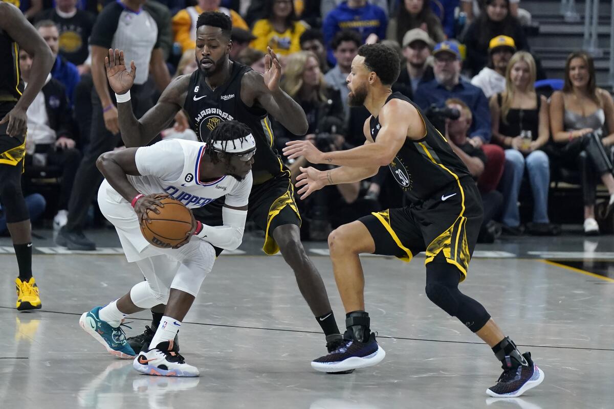Clippers guard Reggie Jackson is defended by Golden State Warriors forward JaMychal Green and guard Stephen Curry.