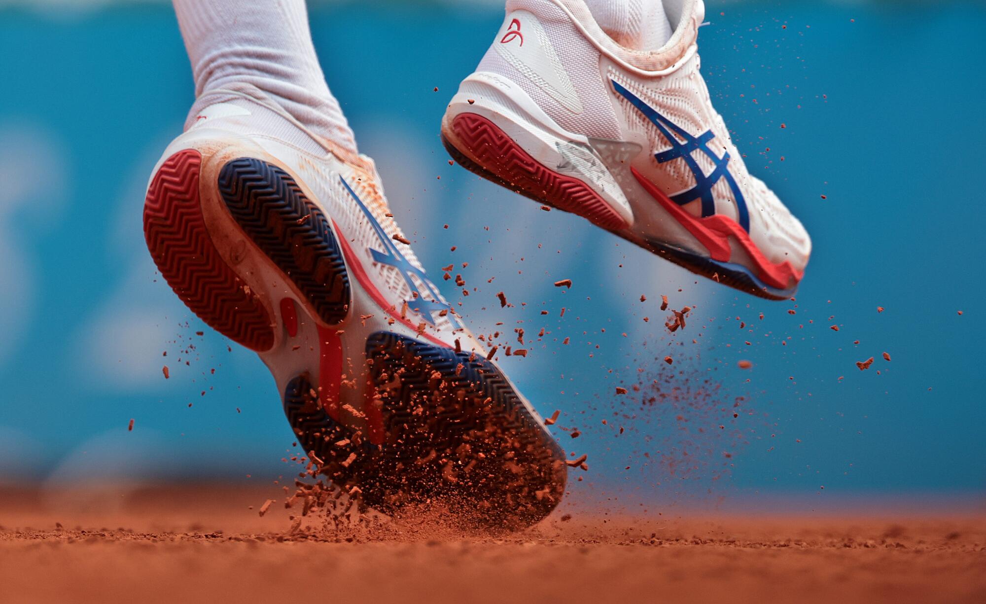 A closeup of Serbian tennis player Nikola Djokovic's shoes kicking up dirts as she serves