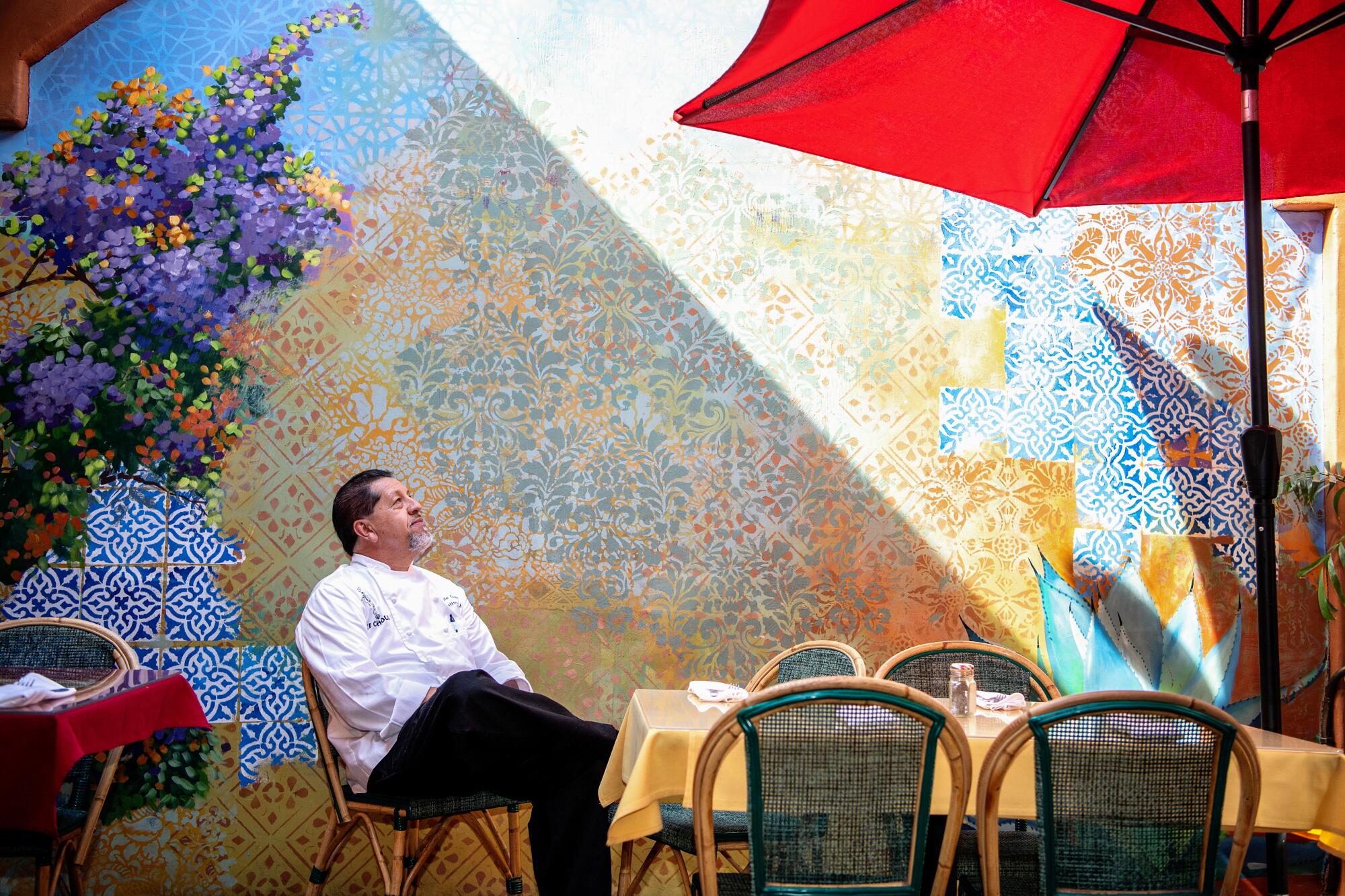 Sergio Ochoa sitting at an outdoor table, in front of an ornate mural.
