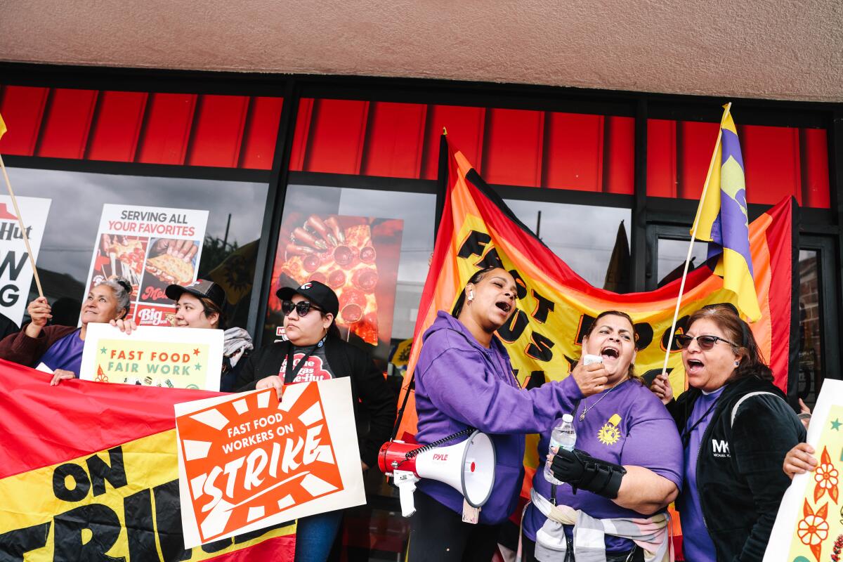 Los Angeles, CA - March 06: Anneisha Williams, third right, Imelda, second right, and Laura Posos, right, chant in support of a three-day strike to protest ongoing wage theft, including the denial of meal breaks, overtime and paid sick leave at Pizza Hut's 2542 W. Temple Street location on Wednesday, March 6, 2024 in Los Angeles, CA. The workers have filed a complaint with the state labor commissioner seeking over $80,000 in back pay and penalties. (Dania Maxwell / Los Angeles Times)