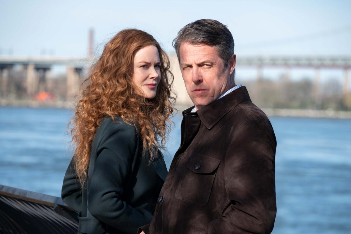 A woman and a man stand along the water with a bridge in the distance