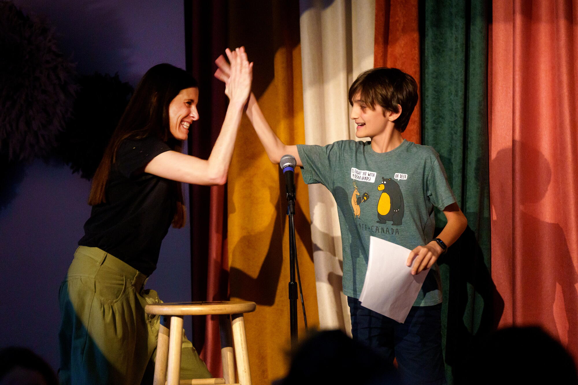 A woman high-fives a young comic on stage.