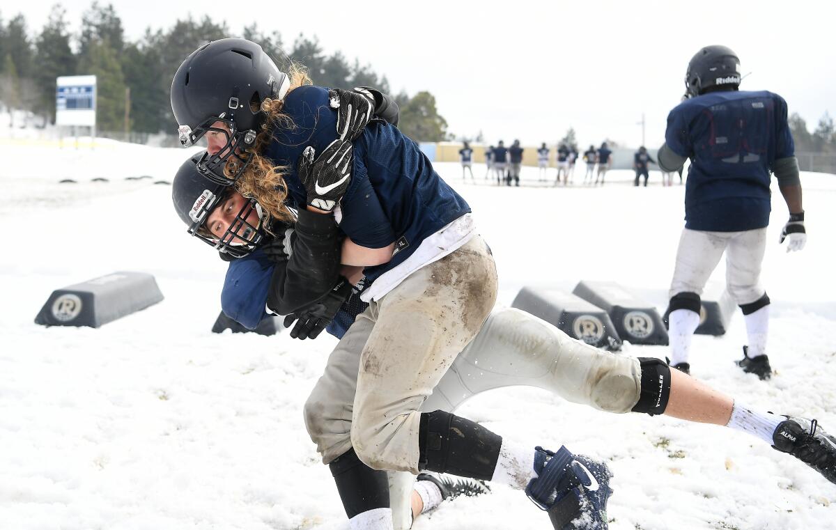 A football player tackles another player in the snow