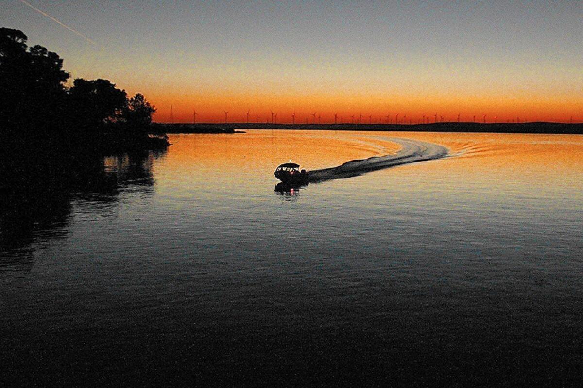 A boat leaves a wake at sunset on a calm, flat body of water.