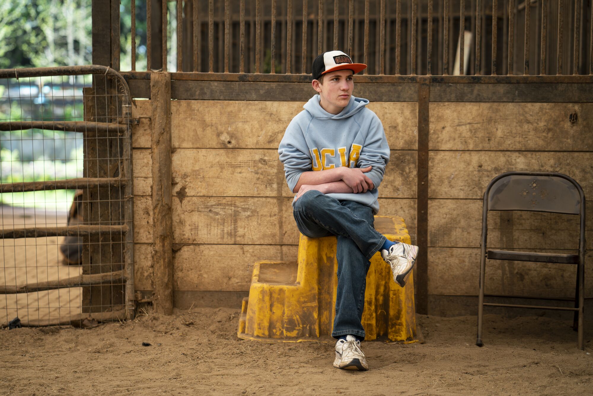 A teenage boy sits on a step near a horse ring.