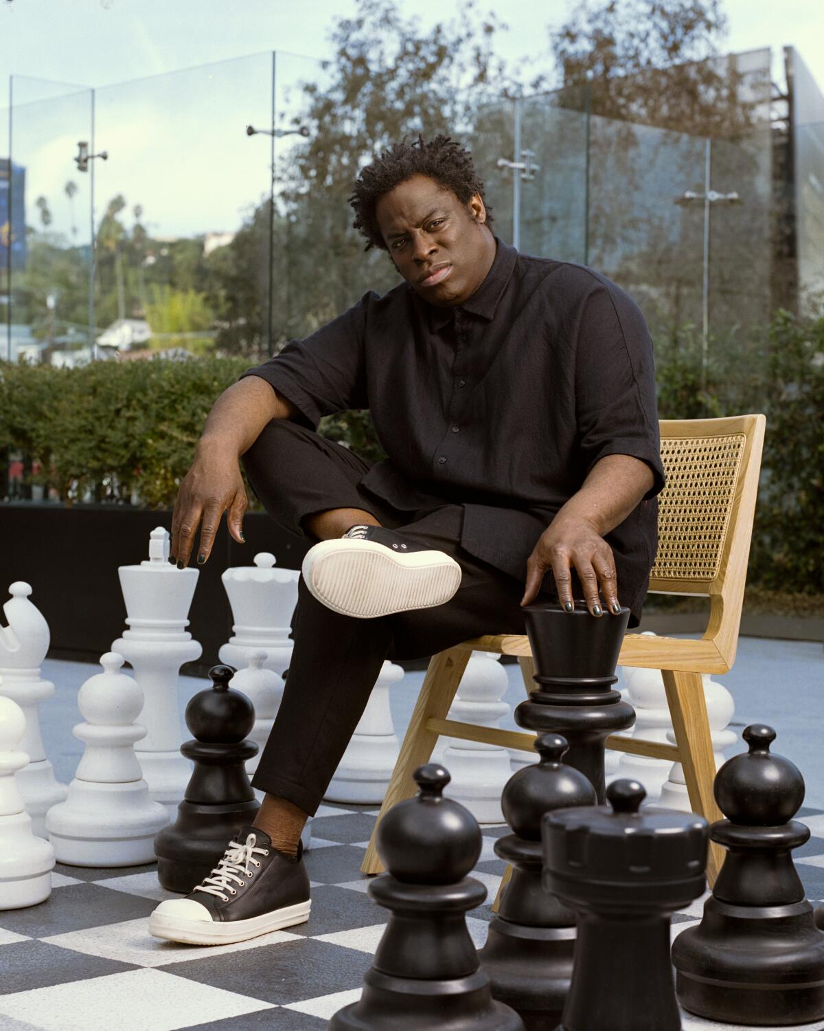 A man sits within a large patio chess set.