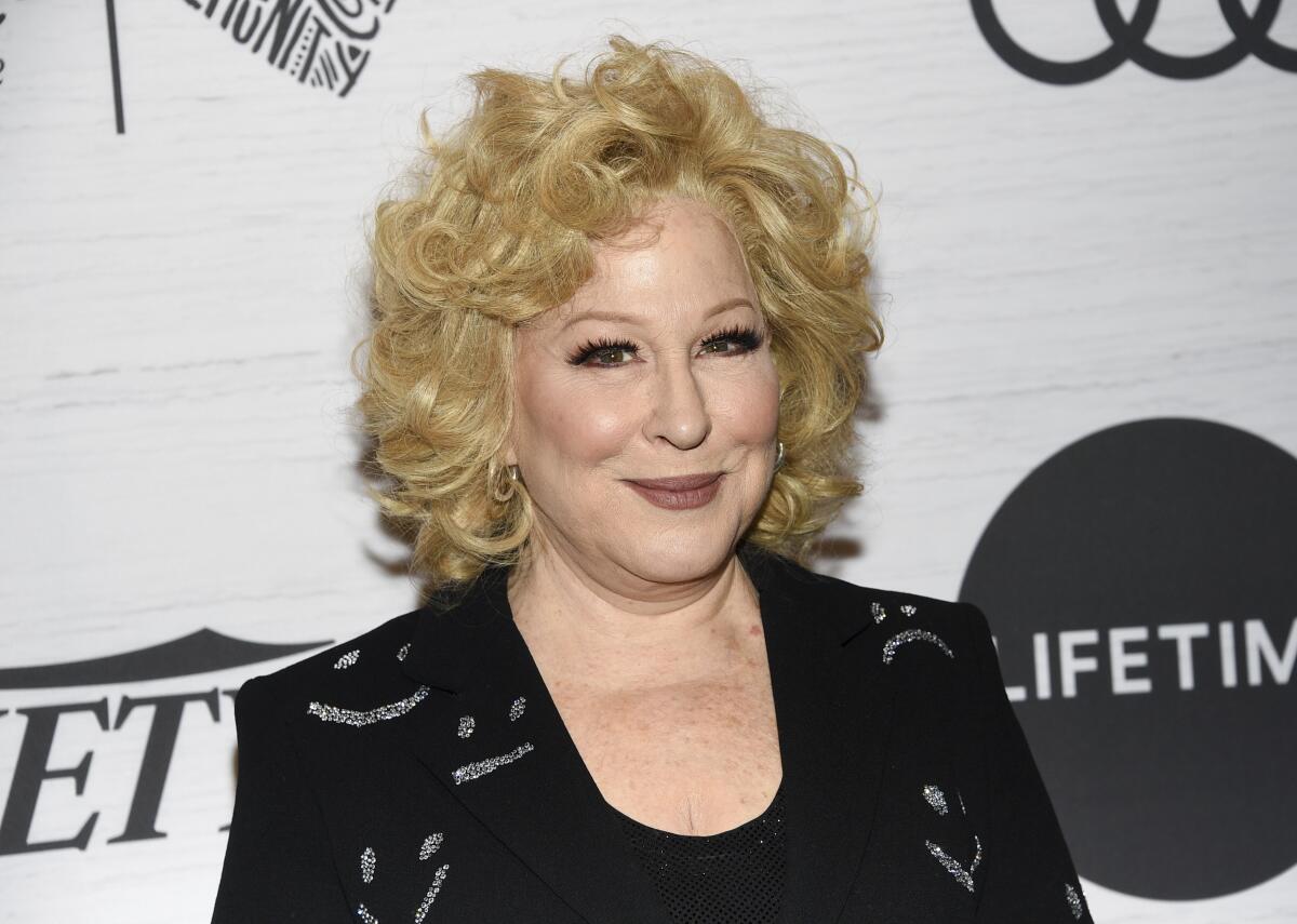 A woman with curly blond hair posing in a black outfit