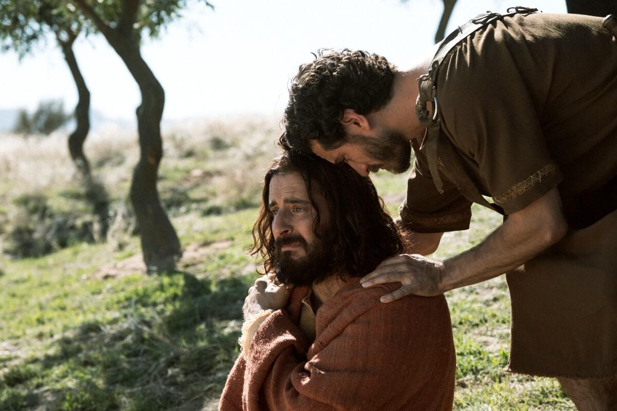 A man crouches over another man on a hillside