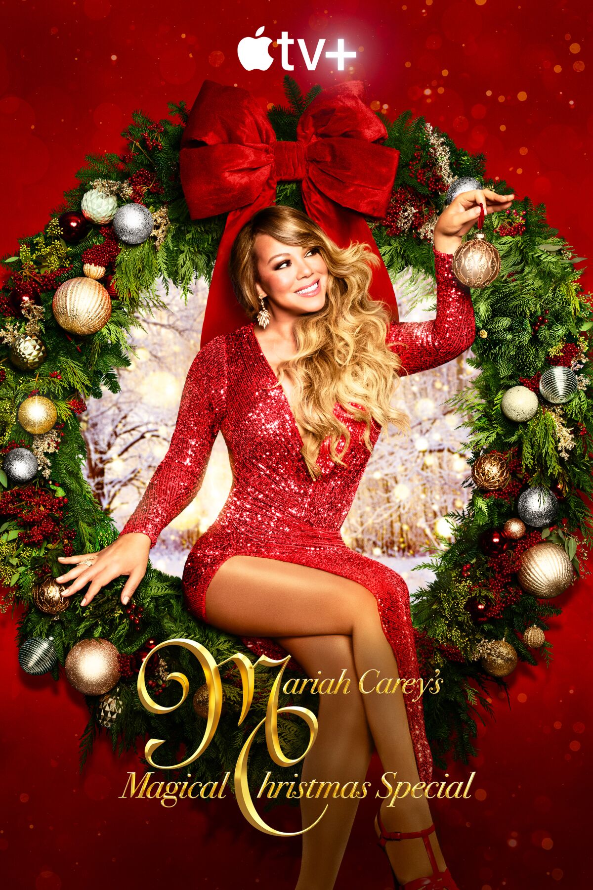 Mariah Carey in a red dress holding an ornament sitting in a Christmas wreath with a snowy woods scene behind her