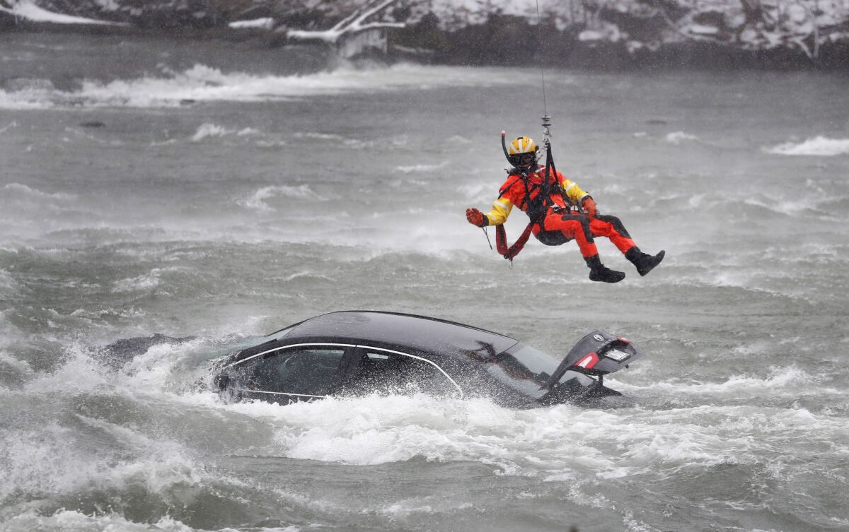 A U.S. Coast Guard diver is lowered from a hovering helicopter to pull a body from a submerged vehicle stuck in rushing rapids just yards from the brink of Niagara Falls, Wednesday, Dec. 8, 2021, in Niagara Falls, N.Y. (Sharon Cantillon/The Buffalo News via AP)