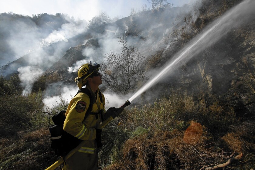 CalFire firefighter Jeff Newby sprays water on smoldering brush burned by the Colby fire along Highway 39 in Azusa on Friday. Gov. Jerry Brown's drought emergency declaration calls on state agencies to hire additional seasonal firefighters this year to respond to elevated wildfire risk.