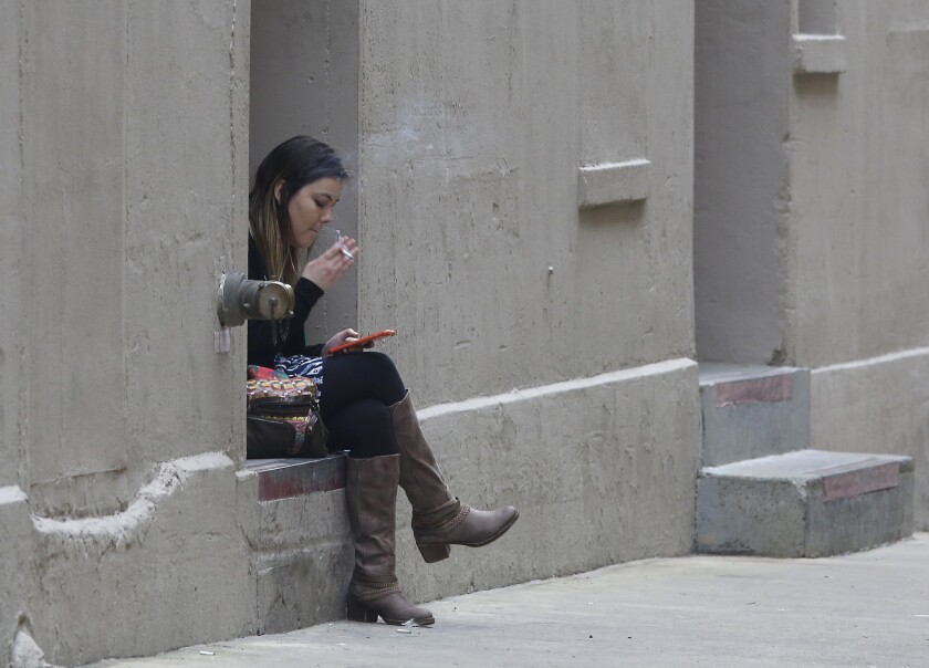 A woman smokes a cigarette while using a smart phone on March 10 in Sacramento. State lawmakers have approved a package of laws to further restrict the use of tobacco in California.