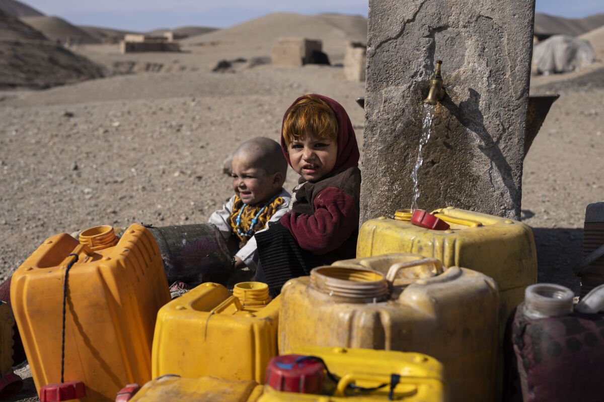 Two Afghan children sit next to a spigot as people of Kamar Kalagh village outside Herat, Afghanistan, try to fill their plastic containers with water, on Friday, Nov. 26, 2021. Afghanistan’s drought, its worst in decades, is now entering its second year, exacerbated by climate change. (AP Photo/Petros Giannakouris)