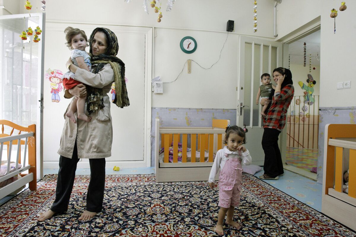 Iranian teachers holding young children in a Tehran kindergarten