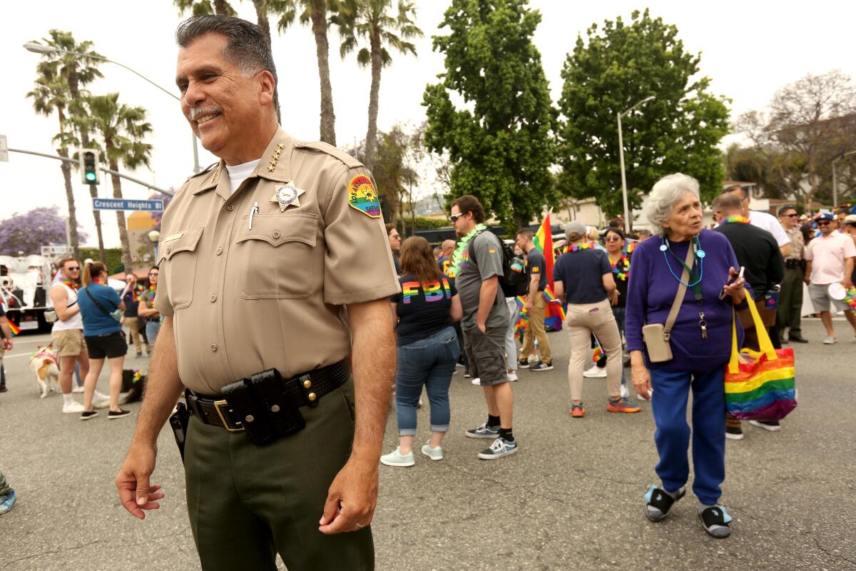 Among a crowd, Los Angeles County Sheriff Robert Luna smiling in uniform with a rainbow-colored patch on his sleeve