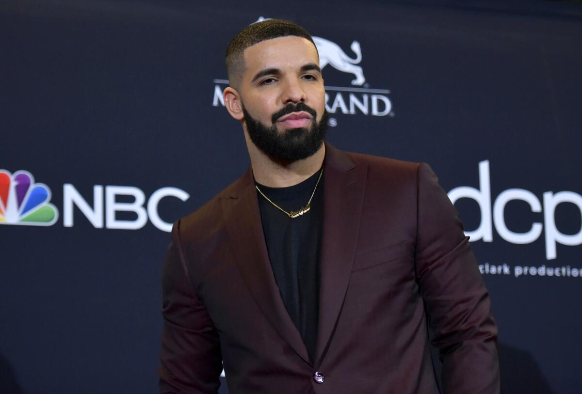 Drake poses for photos at a red carpet event in a burgundy blazer, black shirt and gold necklace