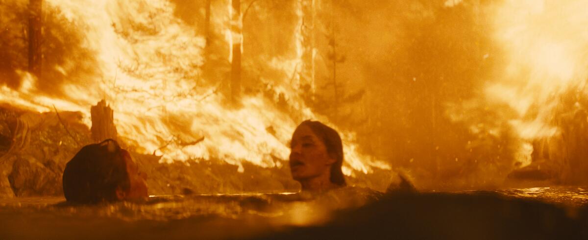 With flames all around, Finn Little's and Angelina Jolie's characters are submerged up to their necks in a lake.