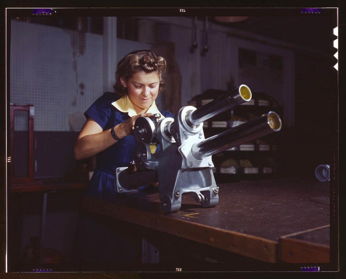 A young female employee of North American Aviation Inc. working over the landing gear mechanism of a P-51 fighter plane in Inglewood. The mechanism resembles a small cannon. October 1942.