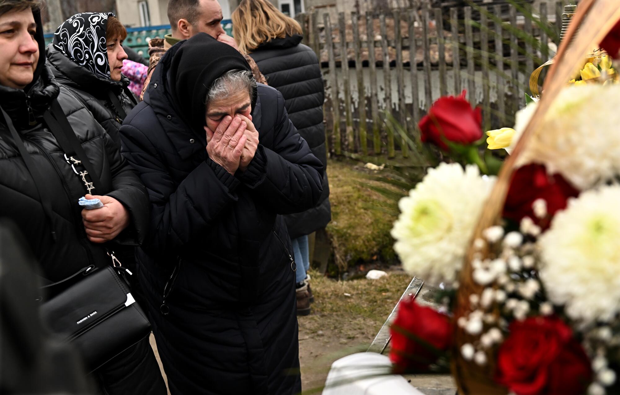 A woman cries in front of a funeral wreath.