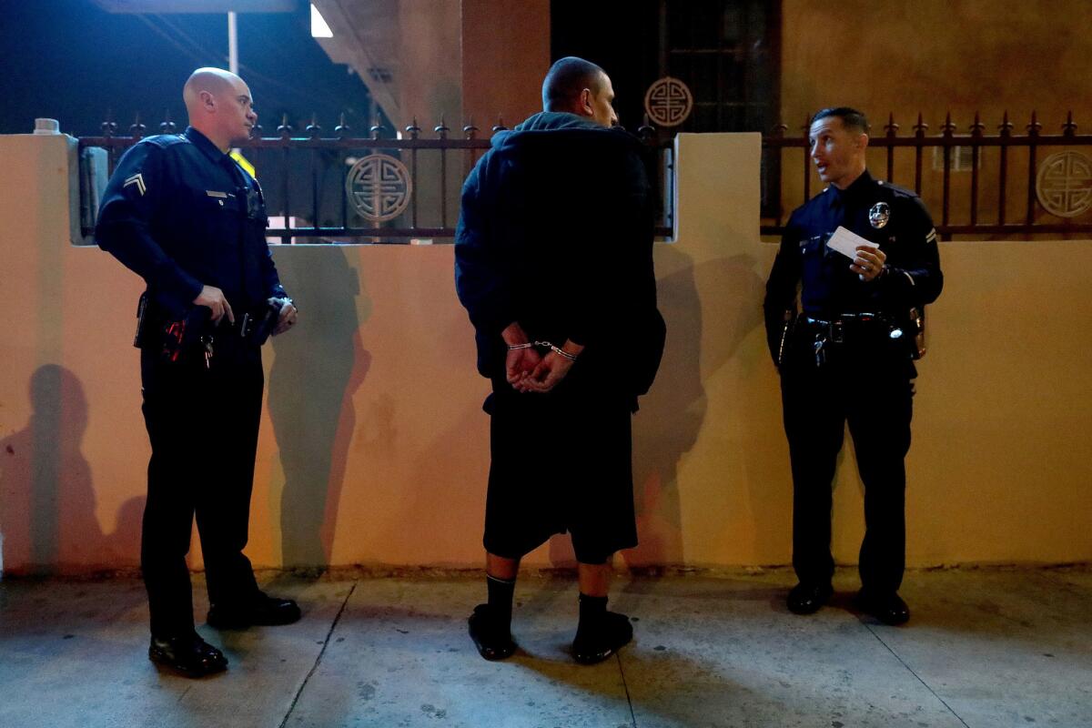 LAPD Metropolitan Division officers Elden Marquez, left, and Eduardo Ojeda detain a suspect whose identification shows a $10,000 traffic warrant for arrest along the 8400 block of Figueroa.