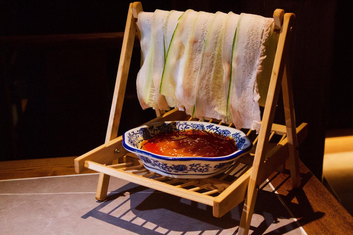 Szechuan Mountain House' signature Swing Pork Belly hangs pork and cucumber slices over a wood dowel above a bowl of sauce.
