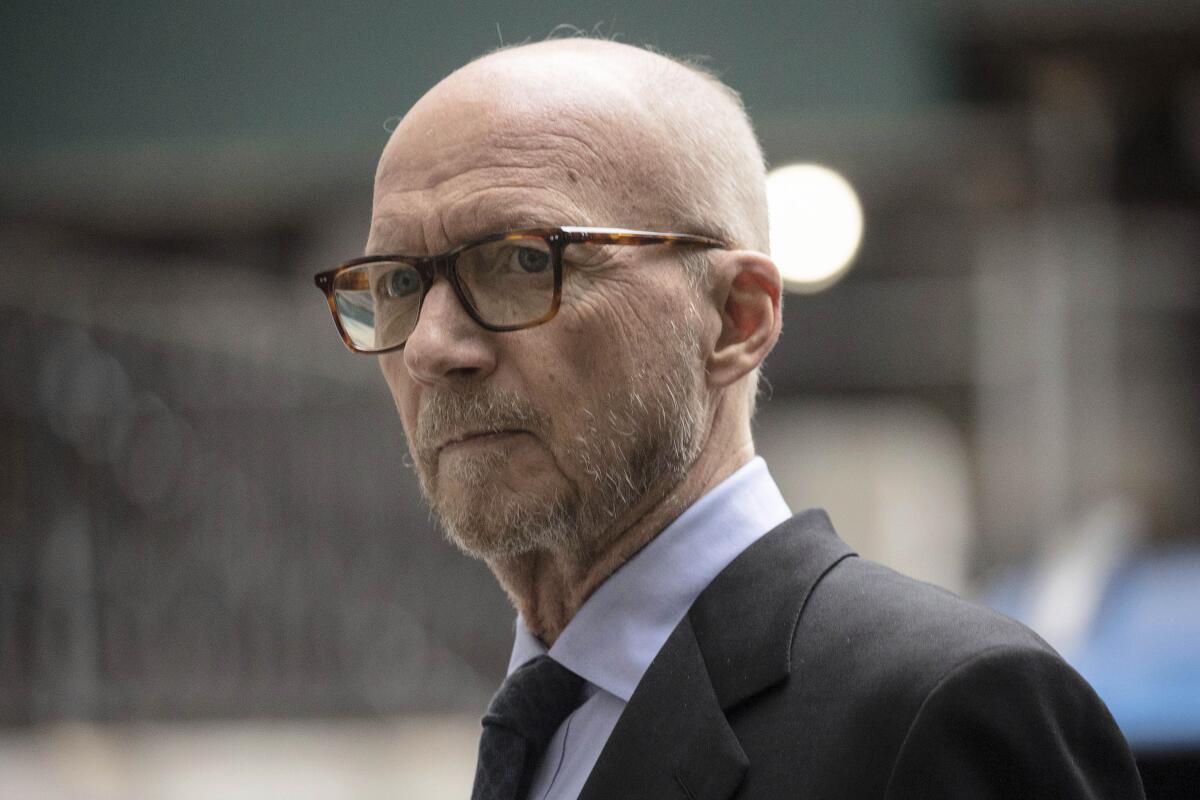 A balding man with facial scruff wears a suit, tie and glasses and looks serious on his way into court