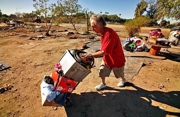 Donald Braden, 49, who has lived for about five months months between the Los Angeles River and the 710 freeway in Lynwood, rushes to move his personal items as crews from the cities of Lynwood and South Gate clean up a homeless encampment.