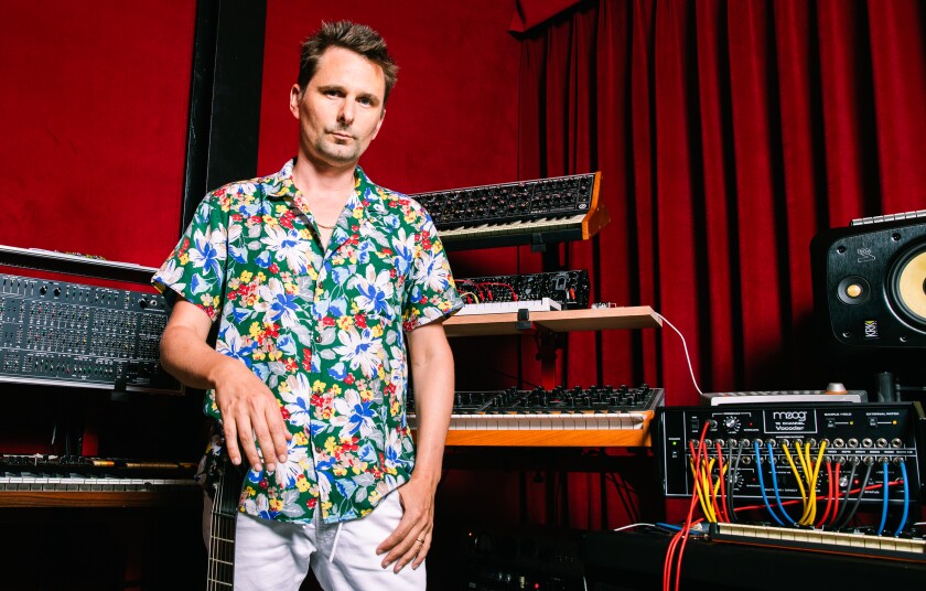 A man in a flowered shirt stands in front of musical instruments in a recording studio