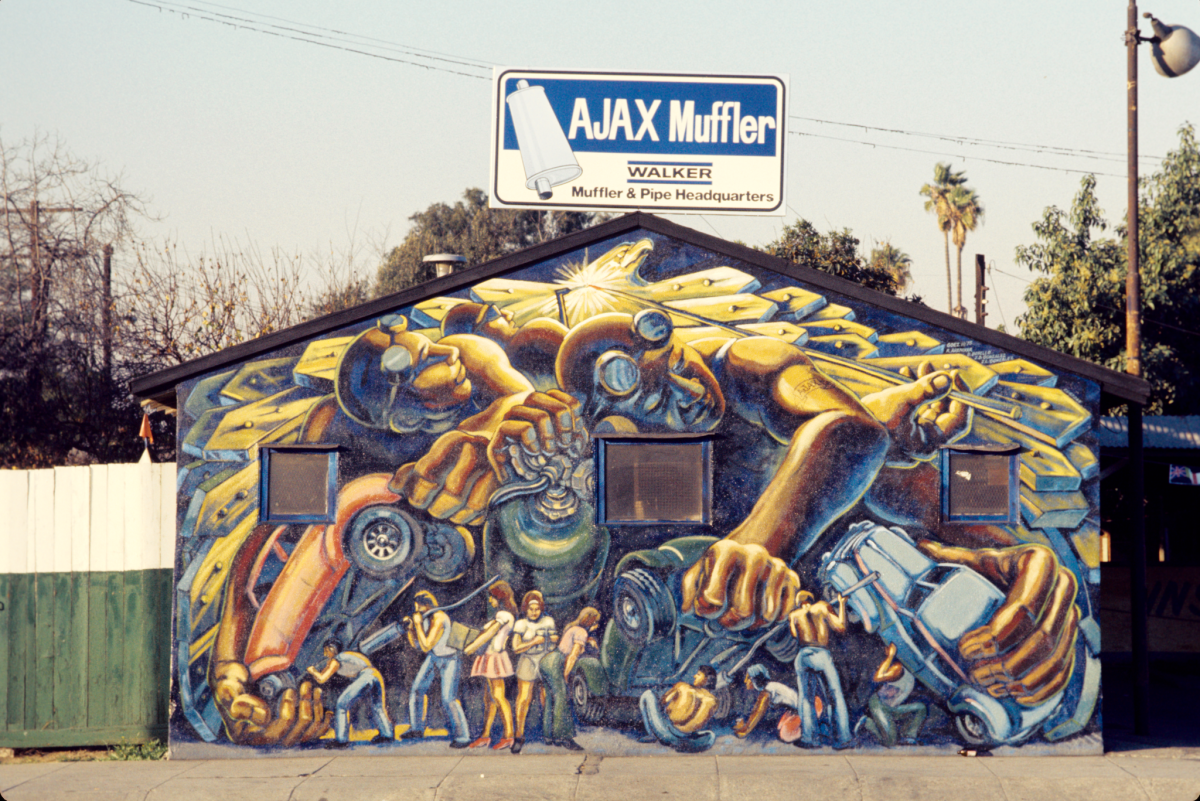 A vintage photograph of a mural shows figures and cars arranged in a mechanical way 