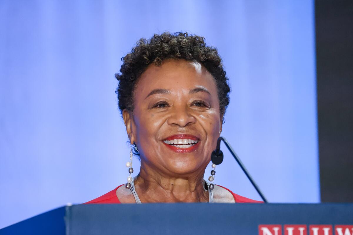 Rep. Barbara Lee smiles while standing behind a podium.