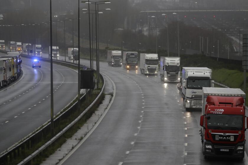 Lorries are escorted by police cars along the M20 away from Dover, England, Monday, Dec. 21, 2020, as part of Operation Stack after the Port of Dover was closed and access to the Eurotunnel terminal suspended following the French government's announcement. France banned all travel from the UK for 48 hours from midnight Sunday, including trucks carrying freight through the tunnel under the English Channel or from the port of Dover on England's south coast. (AP Photo/Kirsty Wigglesworth)