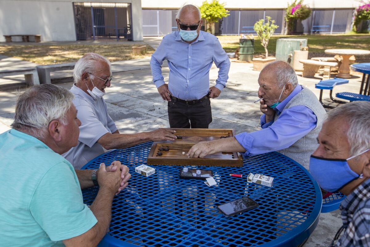 Old friends exhibiting varying degrees of compliance with L.A.'s new face mask policy play backgammon at Reseda Park on Thursday.