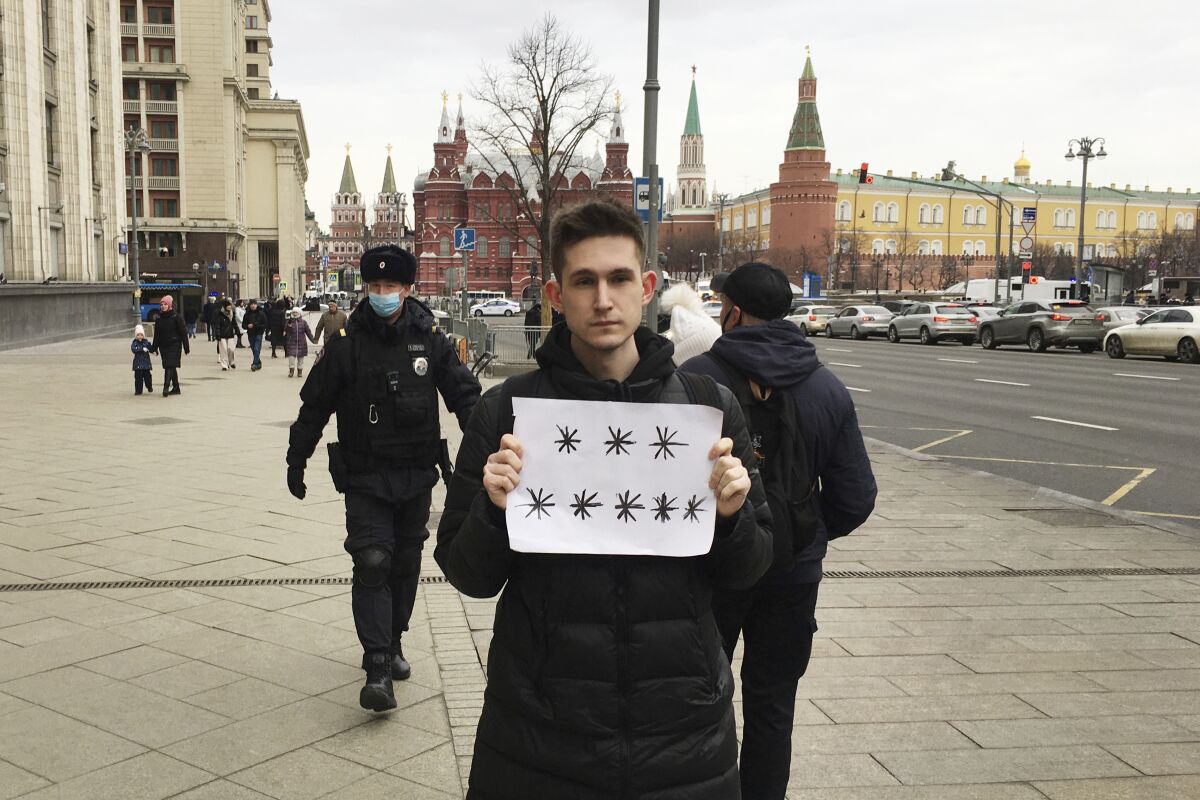 Police officers, left, prepare to detain Dmitry Reznikov holding a blank piece of paper with eight asterisks that could have been interpreted as standing for "No to war" in Russian, with the Kremlin in the background in Moscow, Russia, on Sunday, March 13, 2022. A court found him guilty of discrediting the armed forces and fined him 50,000 rubles ($618) for holding the sign in a demonstration that lasted only seconds before police seized him. (SOTA via AP)