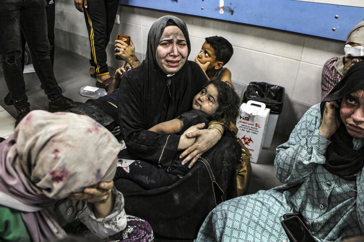 Wounded Palestinians, including a woman holding a child, sit at a hospital in Gaza City.