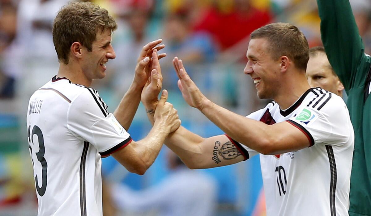 German forward Thomas Mueller, left, is greeted by teammate Lukas Podolski while coming off the field during a substitution in a group game Monday against Ghana. Mueller scored three goals in the 4-0 victory.