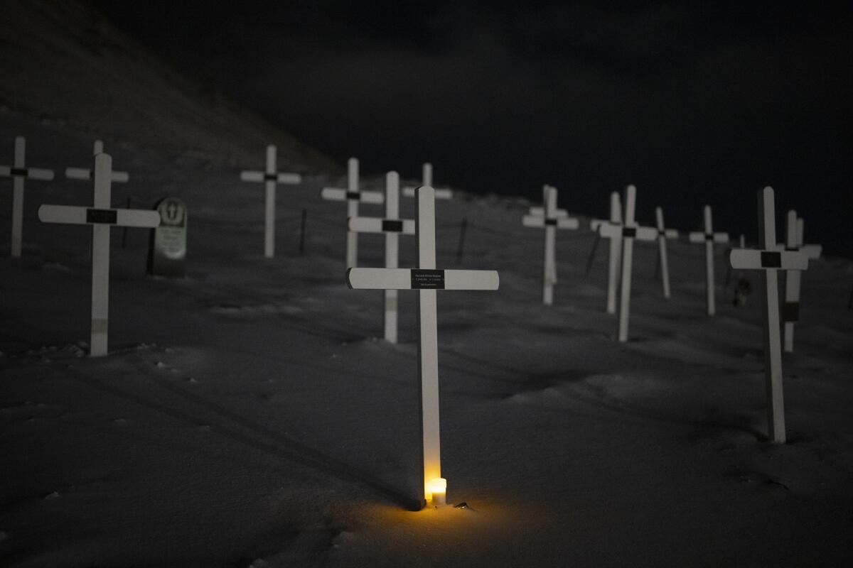 A light glows from the foot of a grave at a cemetery covered in snow.