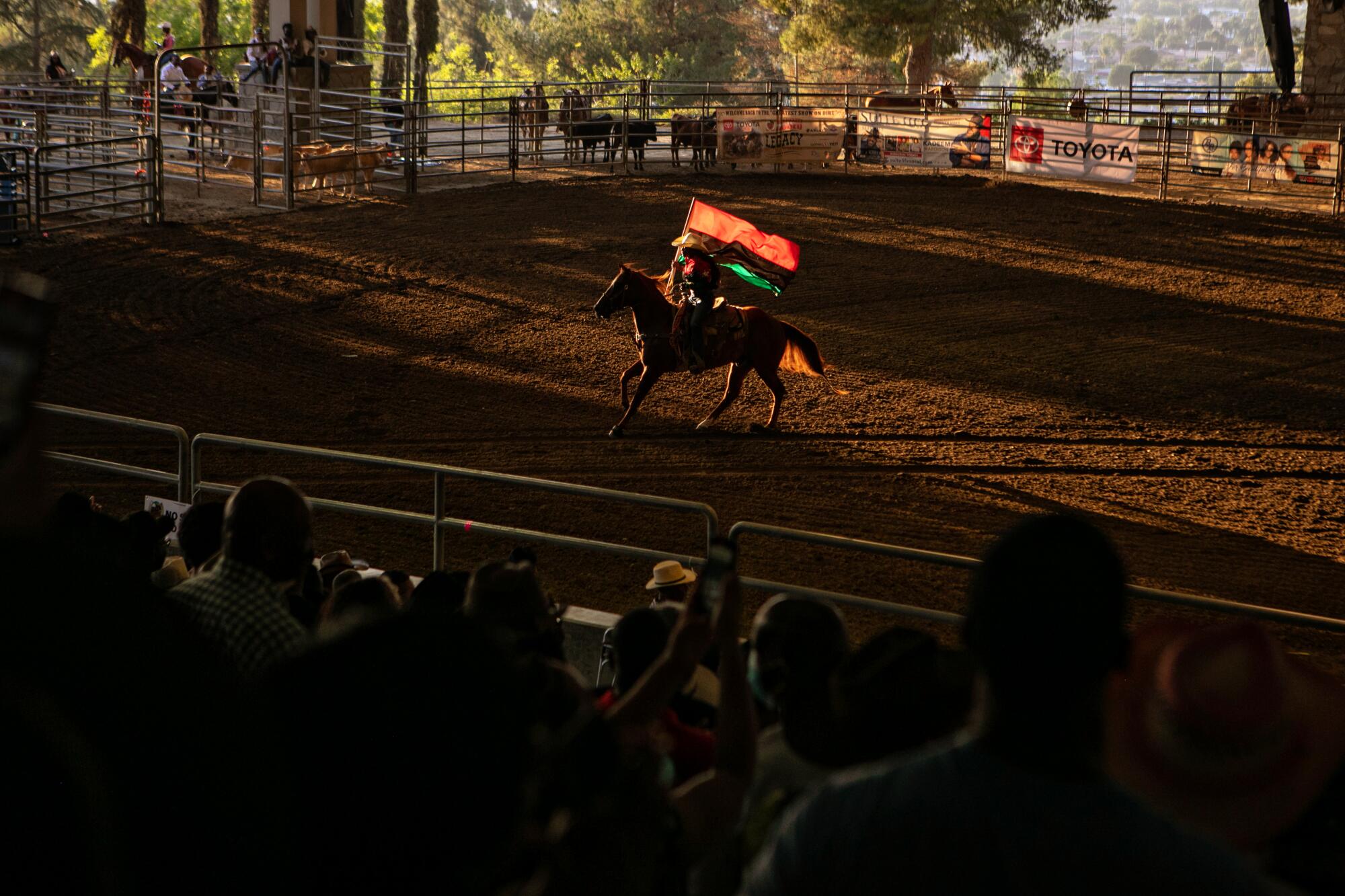 A cowgirl carrying the Pan-African flag as she rides a horse at a rodeo