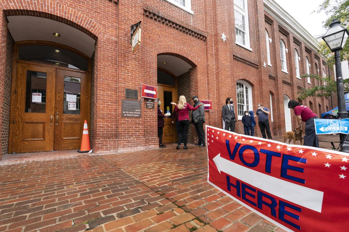 People stand outside a red brick building behind a sign reading "Vote here"